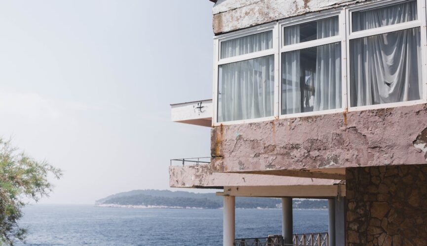 Minimalist luxury home with large floor-to-ceiling windows offering a panoramic view of the ocean under a bright, clear sk...