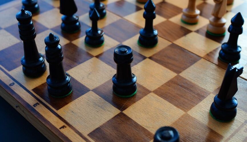 Close-up of a chess board mid-game, with focused lighting on the pieces, representing the strategic showdown between diffe...