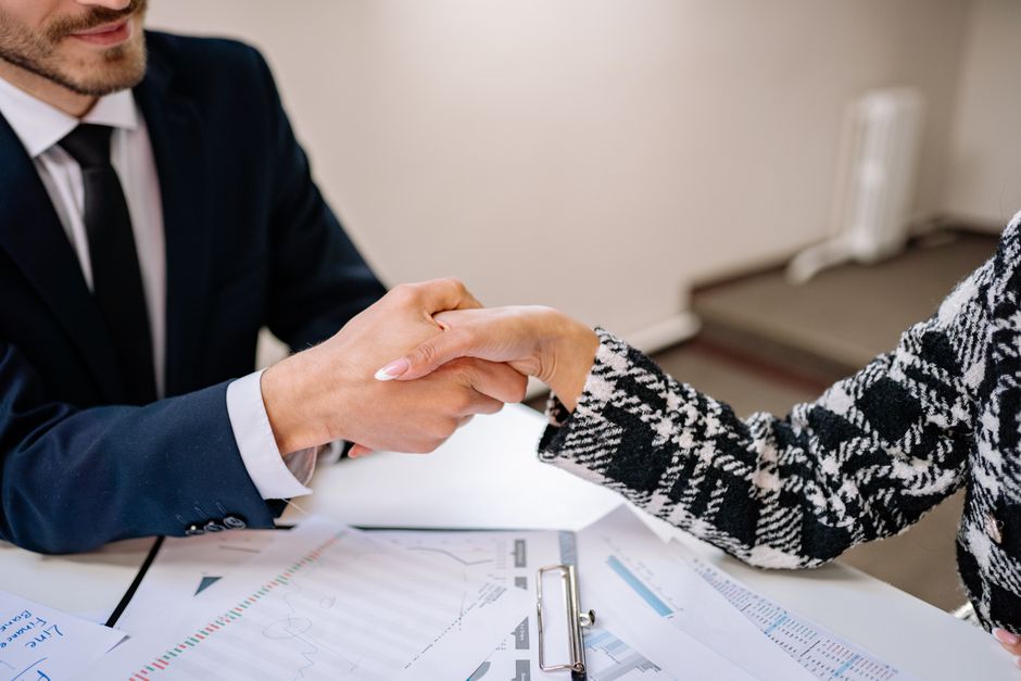 Two professionally dressed individuals shaking hands across a modern table with documents, signifying a clear and successful real estate agreement under new commission structures.